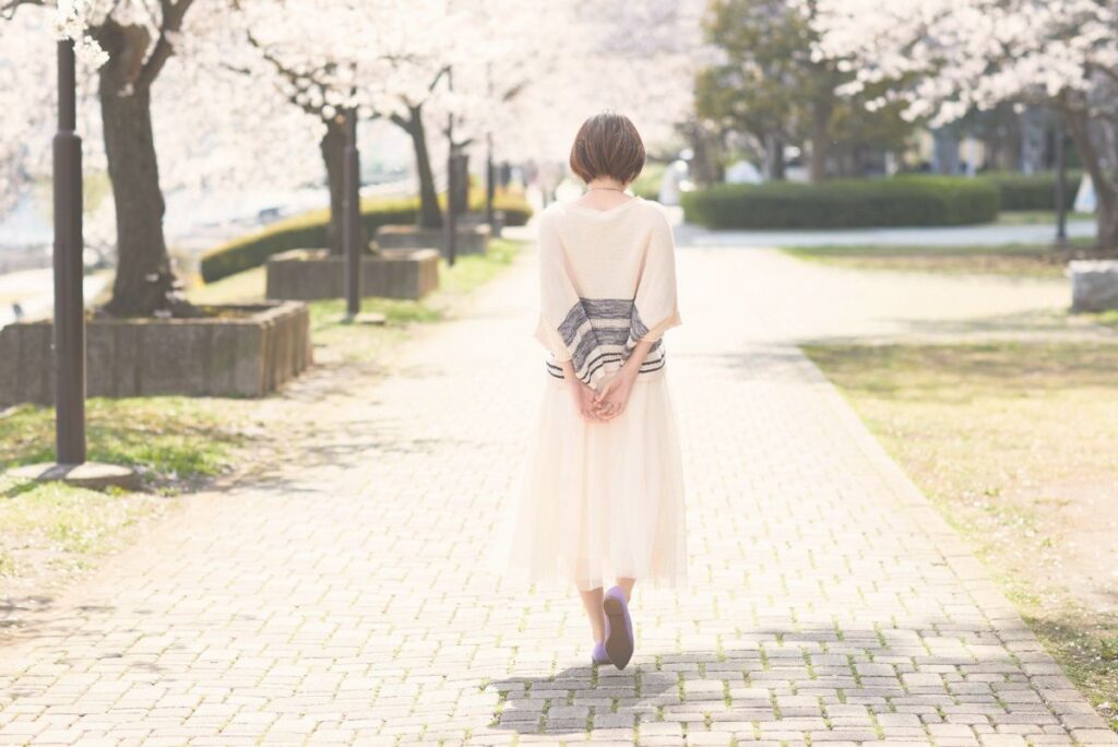 桜並木を自分のペースで歩く女性の後ろ姿。病気を経験したあとの新しい一歩